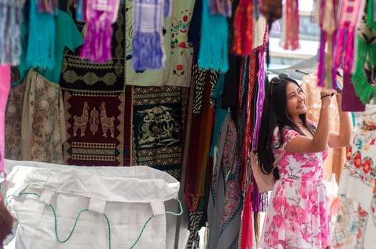 In a bustling open-air market, a woman is seen sightseeing and browsing vibrant fabrics, surrounded by a variety of prints and colors. High quality photo