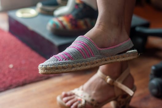 A close-up image captures a womans foot as she slips on a colorful handmade crochet slipper in a cozy indoor setting, highlighting the texture and pattern. High quality photo