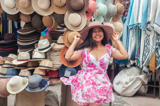 A cheerful young woman is trying on a stylish wide-brimmed hat at a colorful hat stall in an outdoor marketplace, radiating joy and satisfaction. High quality photo