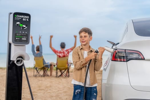 Family vacation trip traveling by the beach with electric car, little boy recharge EV car while his family enjoy seascape beach. Family trip with alternative energy and eco-friendly car. Perpetual