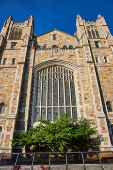 Gothic-style Cathedral at University of Michigan in Ann Arbor, featuring intricate stonework and a grand stained glass window against clear blue sky