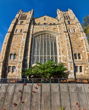 Gothic Revival church with detailed stonework against blue sky at University of Michigan, Ann Arbor, showcasing history amidst urban greenery