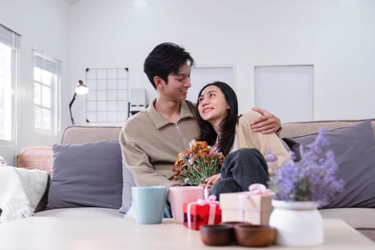 A young Asian couple gives flowers to each other on their anniversary and sits happily together in the living room..