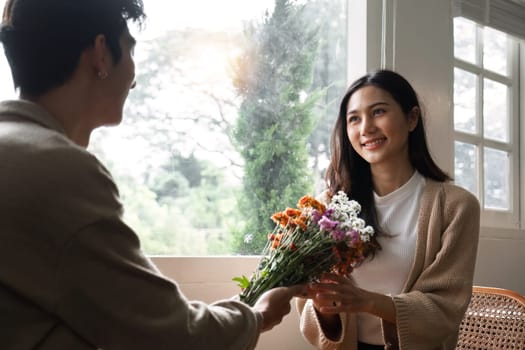 A young Asian couple gives flowers to each other on their anniversary and sits happily together in the living room..