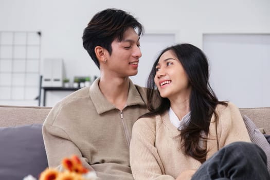 A young Asian couple gives flowers to each other on their anniversary and sits happily together in the living room..