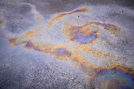 Colorful rainbow stains of an oil spill on wet asphalt.