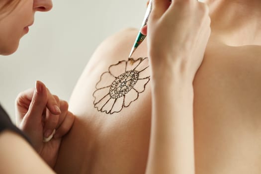 Mehndi master drawing with henna on model's back, close-up