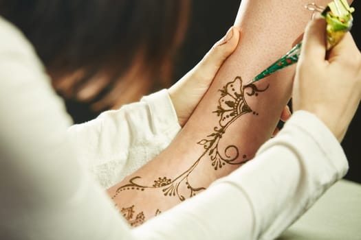 Art of mehndi. Master paints model's leg with henna