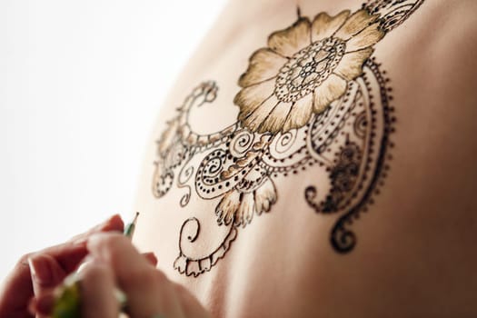 Mehndi. Beautiful henna patterns in process of applying on model's back
