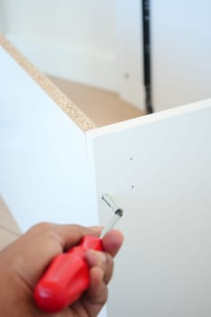 A person is using a screwdriver to screw a screw into a piece of white plastic.