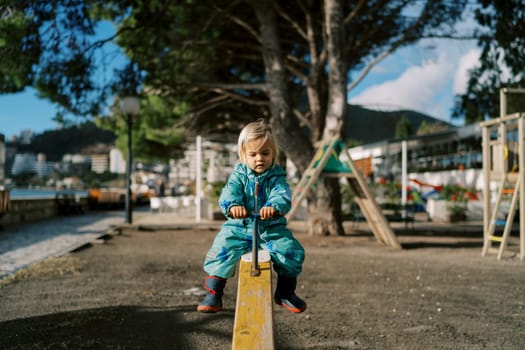 Little girl rides on a wooden swing-balancer holding the handle. High quality photo