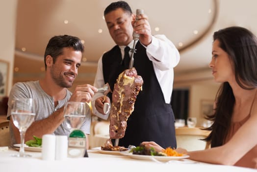 Couple, waiter and service for dinner in restaurant with meat, happiness and fine dining for anniversary or honeymoon. Man, woman and employee with steak on skewer, healthy meal and table in London.