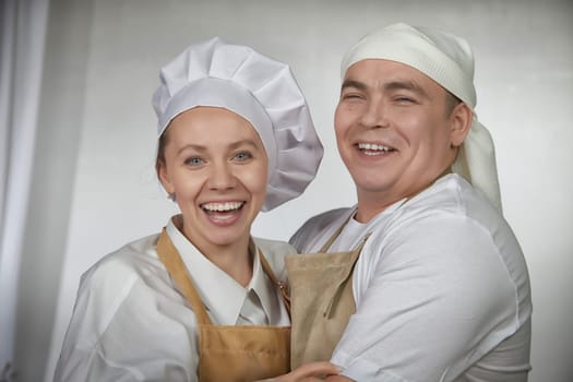 Cute oriental family with wife and husband cooking in kitchen on Ramadan, Kurban-Bairam, Eid al-Adha. Funny couple of cooks at joke photo shoot. Pancakes, pastries, Maslenitsa, Easter