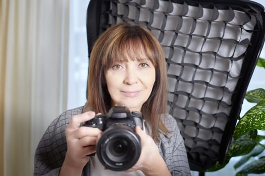 Senior old elderly woman with black camera with a large lens indoors in the studio. Professional photographer. Age Hobby