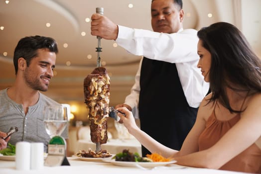 Couple, waiter and service for lunch in restaurant with meat, happiness and fine dining for anniversary or honeymoon. Man, woman and employee with steak on skewer, healthy meal and table in London.