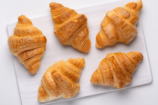 French croissants for breakfast. Freshly baked croissants on cutting board, isolated on white background, top view.