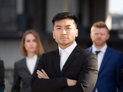 Close up portrait of confident business asian man standing in front of his multiethnic team and looking at camera.