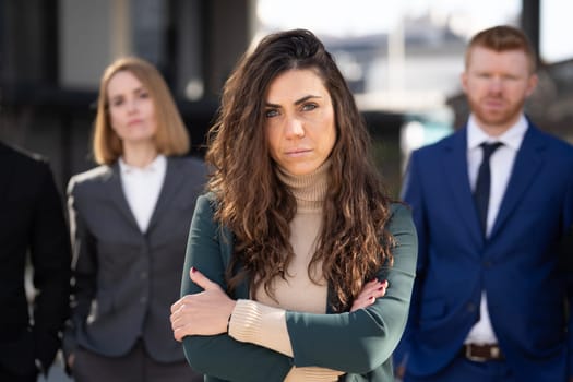 Close up portrait of confident business woman standing in front of her multiethnic team outside while looking at camera.