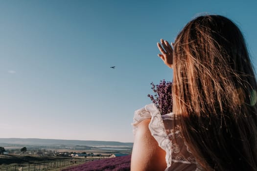 Close up portrait of young beautiful woman in a white dress and a hat is walking in the lavender field and smelling lavender bouquet.