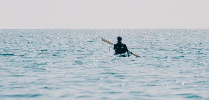 Happy smiling woman in kayak on ocean, paddling with wooden oar. Calm sea water and horizon in background