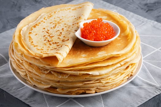 Pancakes with red caviar on grey background.