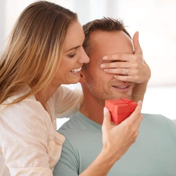 Wife surprise or gift for husband in home and eyes closed for happy couple to celebrate love on couch. Woman, care and giving a present to man, romantic and bonding together on sofa on anniversary.