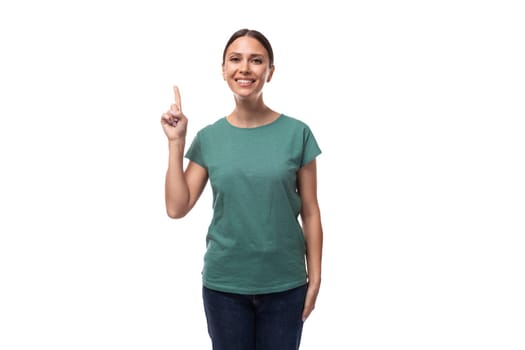 young dreamy beautiful brunette lady with ponytail hairstyle dressed in green t-shirt and jeans holding thumbs up.