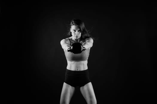 Woman in sportswear doing crossfit workout with kettle bell on a dark yellow red background.