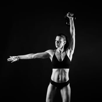 Woman in sportswear doing crossfit workout with kettle bell on a dark yellow red background.