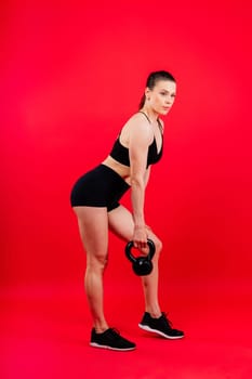 Woman in sportswear doing crossfit workout with kettle bell on a dark yellow red background.