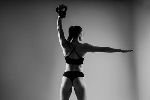 Woman in sportswear doing crossfit workout with kettle bell on a dark yellow red background.