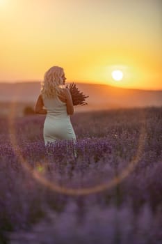 Blonde woman poses in lavender field at sunset. Happy woman in white dress holds lavender bouquet. Aromatherapy concept, lavender oil, photo session in lavender.