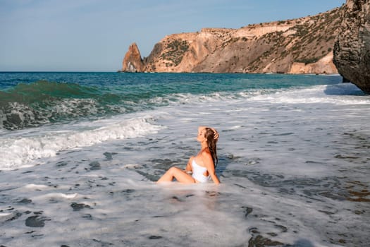 Happy woman in bikini sits on the sea beach. Tanned girl sunbathing on a beautiful shore. Summer vacation or holiday travel concept.