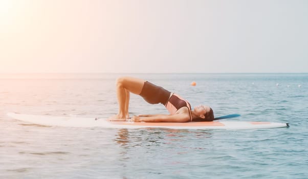 Woman sup yoga. Happy young sporty woman practising yoga pilates on paddle sup surfboard. Female stretching doing workout on sea water. Modern individual female outdoor summer sport activity