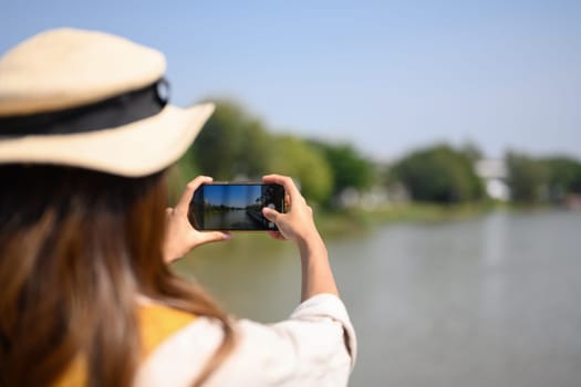 Traveller with backpack taking photo with smartphone on a bridge over a canal.