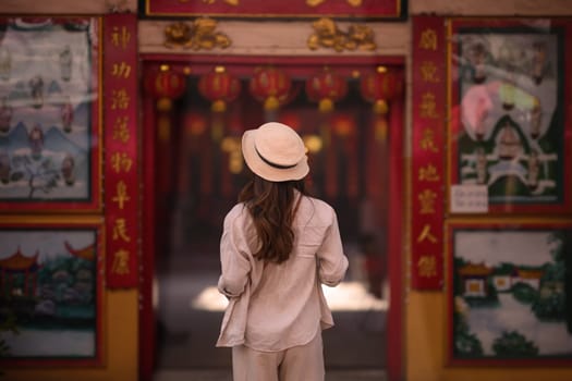 Back view of female tourist strolling inside ancient a Chinese temple with beautiful red lanterns.