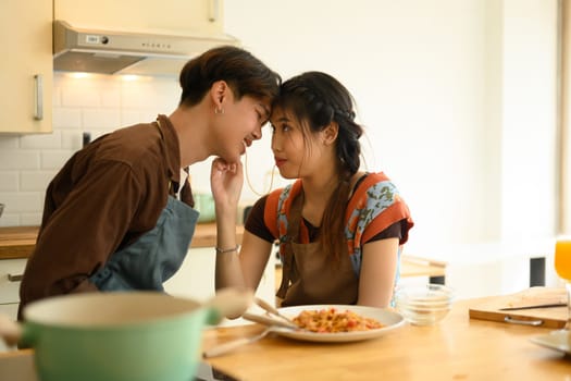 Loving young couple having dinner in kitchen, eating spaghetti. People, relationships and food concept.