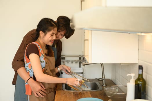 Lovely young couple washing dishes together in the kitchen. Housework, relationship and lifestyle concept.