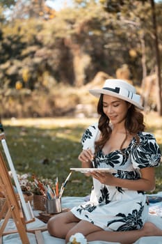 Beautiful young woman painting a picture on an easel in autumn park. Art therapy and creative hobbies concept.