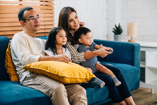 Enjoying family time a young family sits together on the sofa watching TV at home. Laughter fills the room as the father mother brother and sister bond radiating happiness and togetherness.