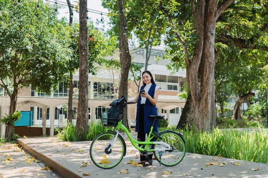 Asian young businesswoman bike to work for eco friendly green energy and use smart phone while commuting in city. Eco friendly.