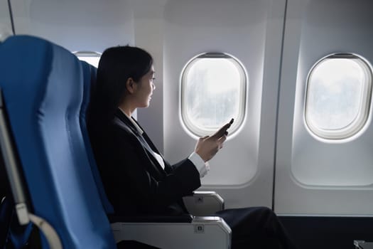 Beautiful Asian businesswoman using mobile phone in aeroplane. working, travel, business concept.
