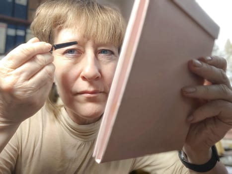 Portrait of a middle-aged woman doing eye makeup. Selfie portrait of lady who is businesswoman, accountant, manager, freelancer doing morning makeup at office on working place