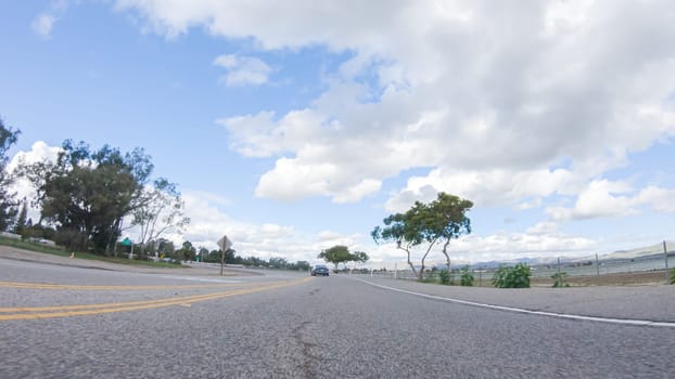 On a clear winter day, a car smoothly travels along Highway 101 near Santa Maria, California, under a brilliant blue sky, surrounded by a blend of greenery and golden hues.