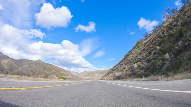 Vehicle is cruising along the Cuyama Highway under the bright sun. The surrounding landscape is illuminated by the radiant sunshine, creating a picturesque and inviting scene as the car travels through this captivating area.