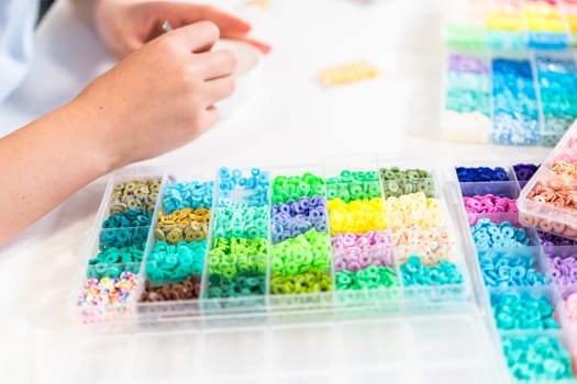 Little girl enjoys crafting colorful bracelets with vibrant clay beads set.