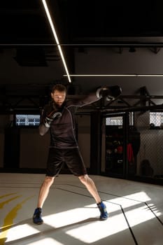 Concentrated boxer engaging in vigorous shadow boxing session in empty dimly gym, simulating fight to enhance strategic combat skills, improve punching technique and maneuvering