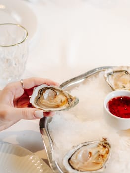 Woman having oysters at table. Fresh oysters on large plate with ice and lemon. Healthy food, gourmet food, restaurant food. Mediterranean cuisine, girl eats, oysters on ice