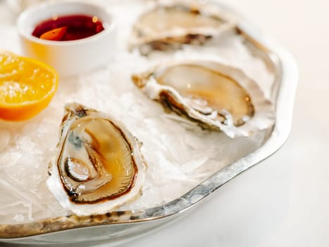 Woman having oysters at table. Fresh oysters on large plate with ice and lemon. Healthy food, gourmet food, restaurant food. Mediterranean cuisine, girl eats, oysters on ice