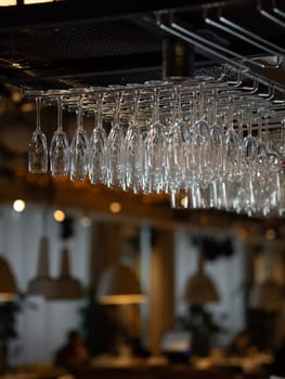 Row of clean glass in bar. Moody aesthetic image of bar and restaurant atmosphere with warm lightening and mane empty wine glasses. Row of clean polished wineglasses hanging in modern bar
